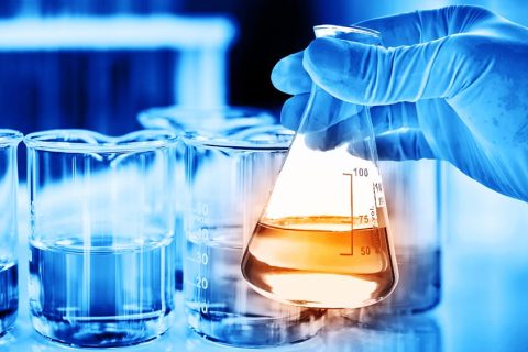 Flask in scientist hand with lab glassware background in laborat